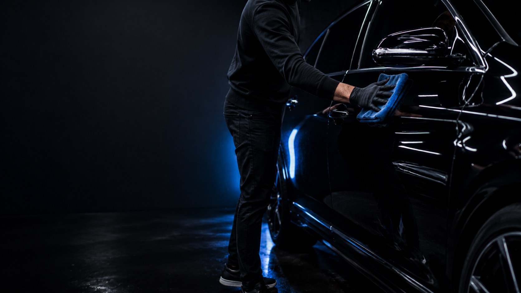 Detailer wiping glossy black car with blue microfiber towel